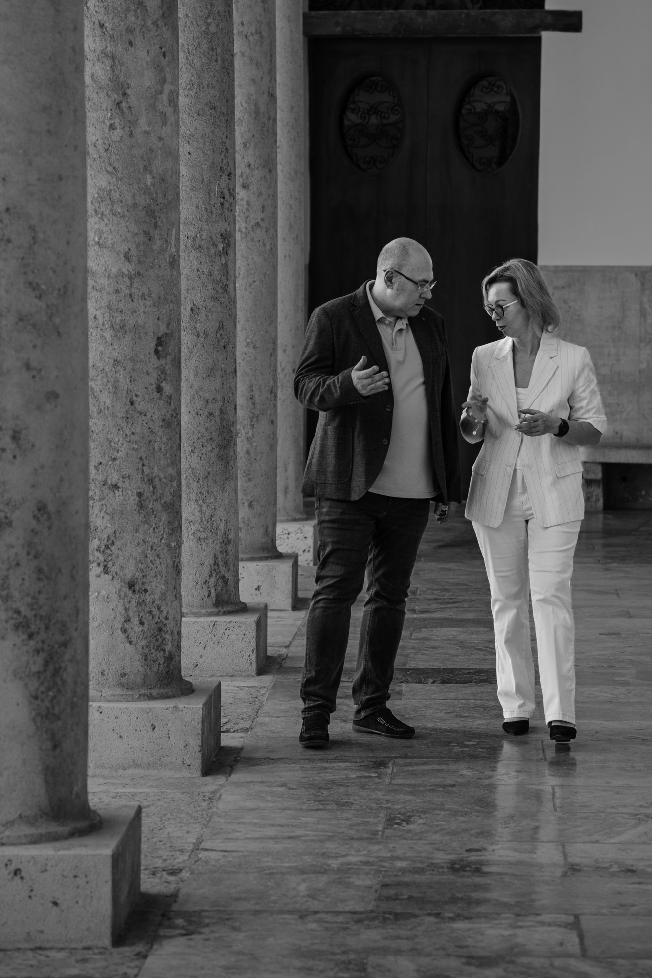 Елена Розина и Виктор Алпер разговаривают во время прогулки вдоль архитектурной колоннады.